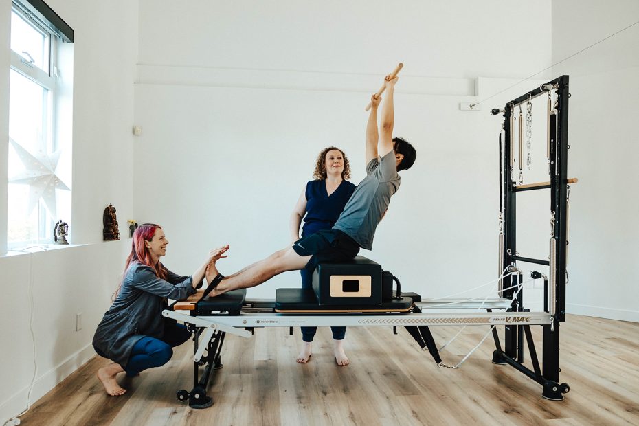 A client doing an exercise on a pilates reformer with assistance from two Embodied staff